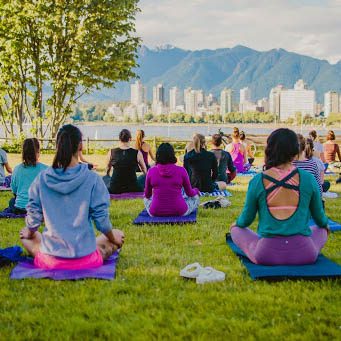 Group of women doing yoga outdoors with downtown Vancouver in the background.