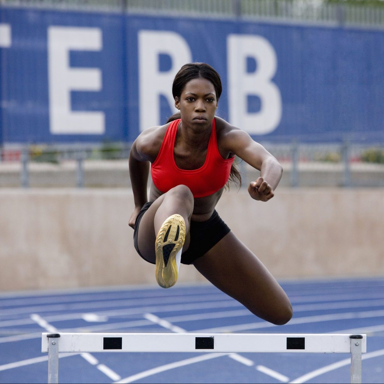 Woman in red sports bra jumps over hurdle.